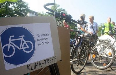 Auf dem Bild ist ein Fahrrad und davor ein Schild mit der Aufschrift "Für sichere Radwege zur Schule"