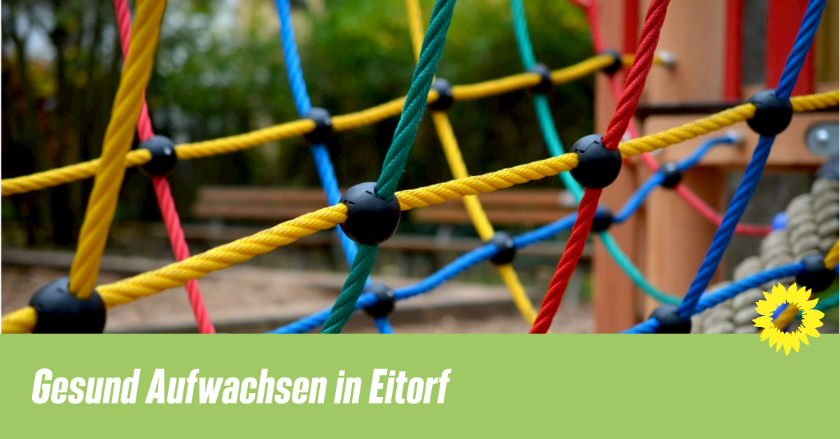 Auf dem Bild ist das Bunte Netz eines Klettergerüstes auf einem Spielplatz zu erkennen. Davor ein grüner Banner, auf dem folgendes steht: "Gesund Aufwachsen in Eitorf"